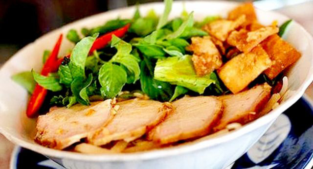 
A bowl includes fresh rice noodles, slices of barbecued pork, bean sprouts, lettuce, and aromatic herbs.
