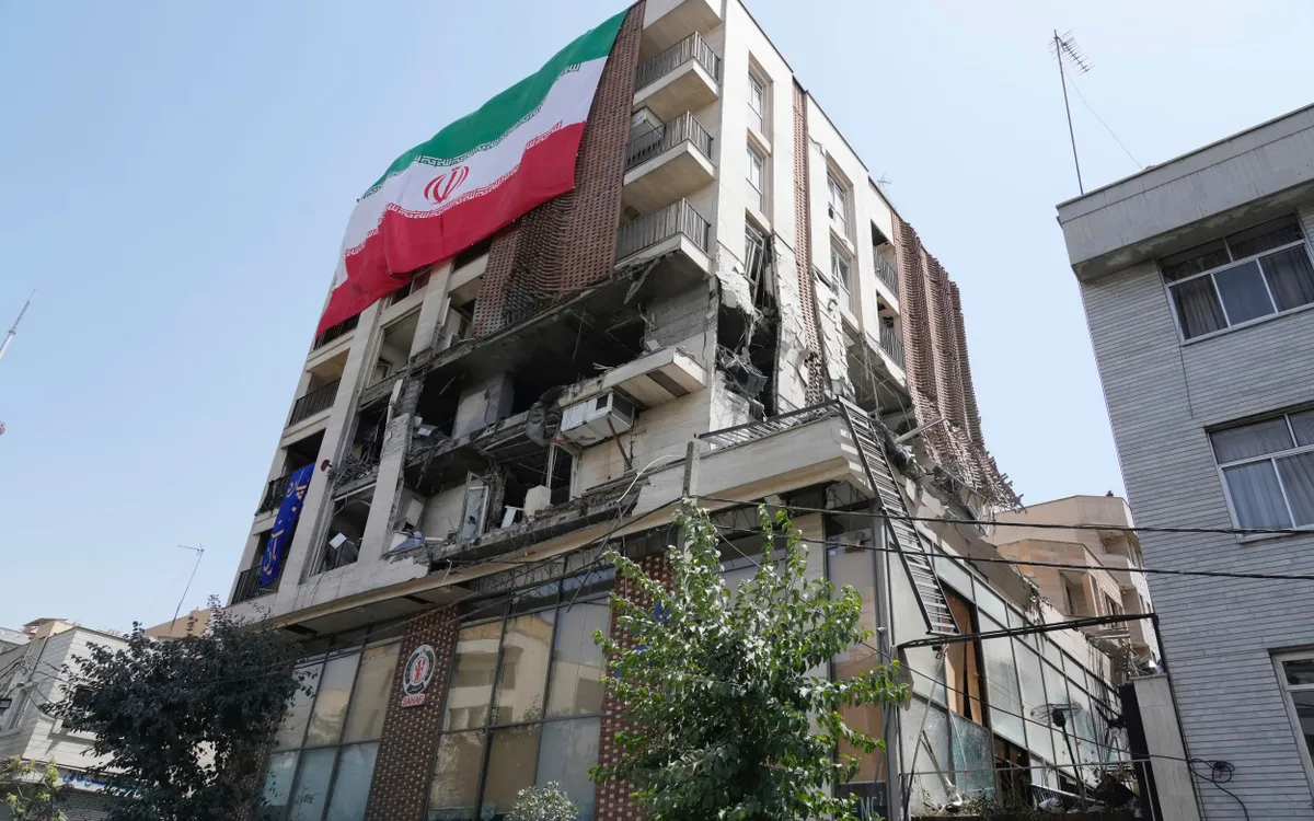 Một lá cờ Iran treo trên một tòa nhà tại Tehran bị trúng đòn không kích của Israel, ngày 25/6/2025 (Ảnh AP)