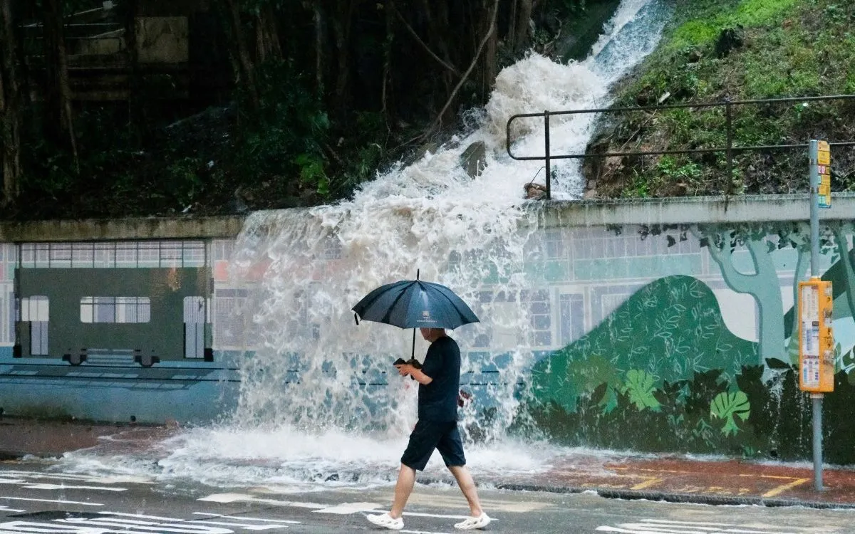 Người đi bộ qua cống tràn nước trên phố ở khu Quarry Bay, Hong Kong, Trung Quốc ngày 5/8/2025, khi cảnh báo mưa bão mức cao nhất được ban hành (Ảnh: AFP)