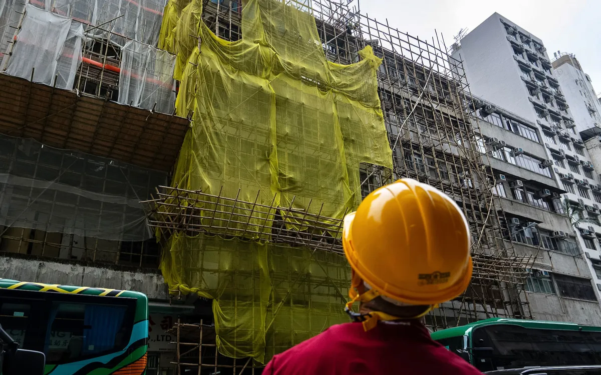 Công nhân đứng gần một tòa nhà đang cải tạo tại khu Mong Kok sau vụ cháy ngày 26/11 ở Wang Fuk Court, Hong Kong, ngày 4/12/2025. (Ảnh: AP)