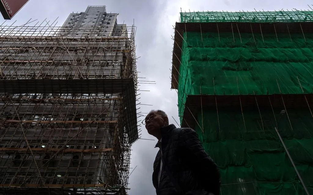 Người đi bộ ngang tòa nhà đang sửa chữa tại Mong Kok sau vụ cháy ngày 26/11 tại Wang Fuk Court ở quận Tai Po, Hong Kong (Trung Quốc), ngày 4/12/2025. (Ảnh: AP)