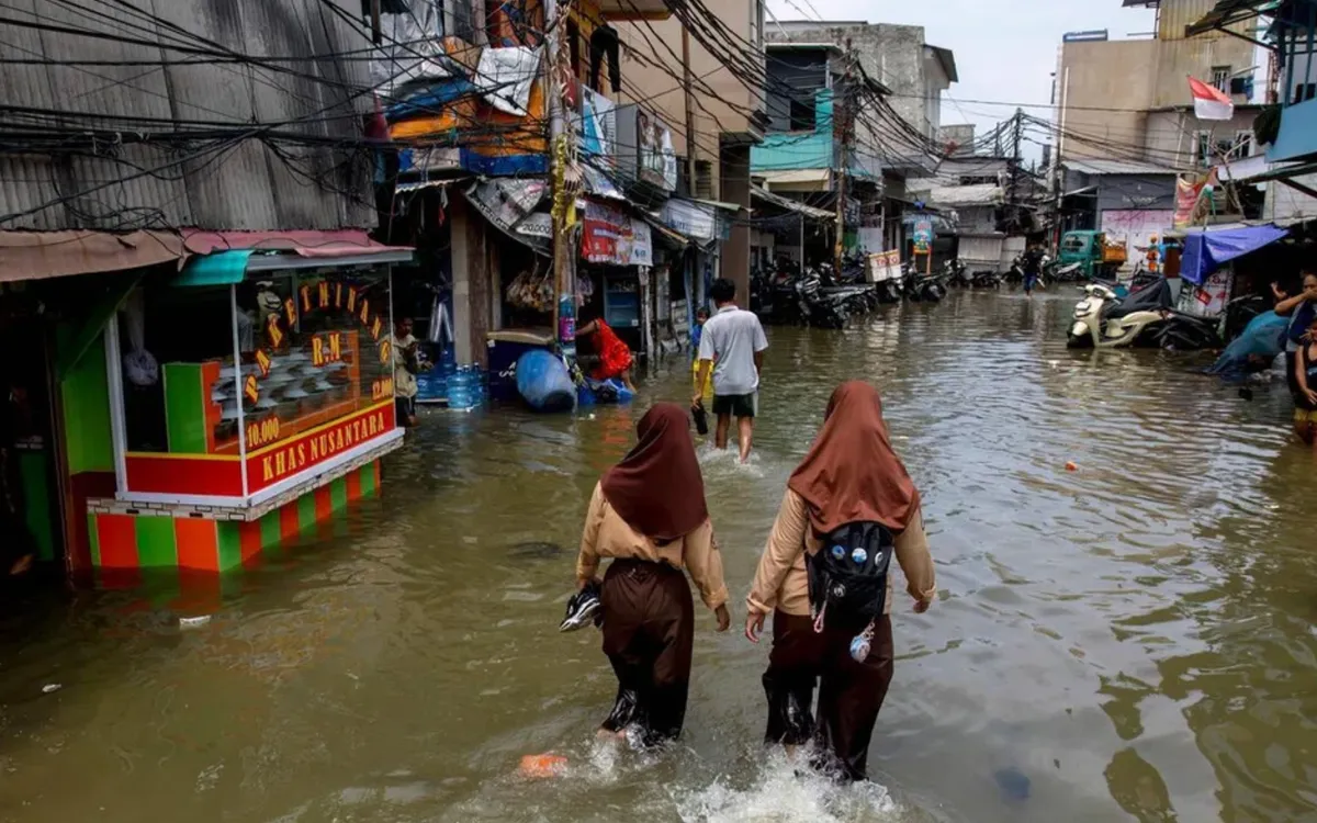 Hai nữ sinh lội qua con phố ngập nước do triều cường ở Muara Baru, Jakarta, ngày 6/12/2025 (Ảnh: AFP)