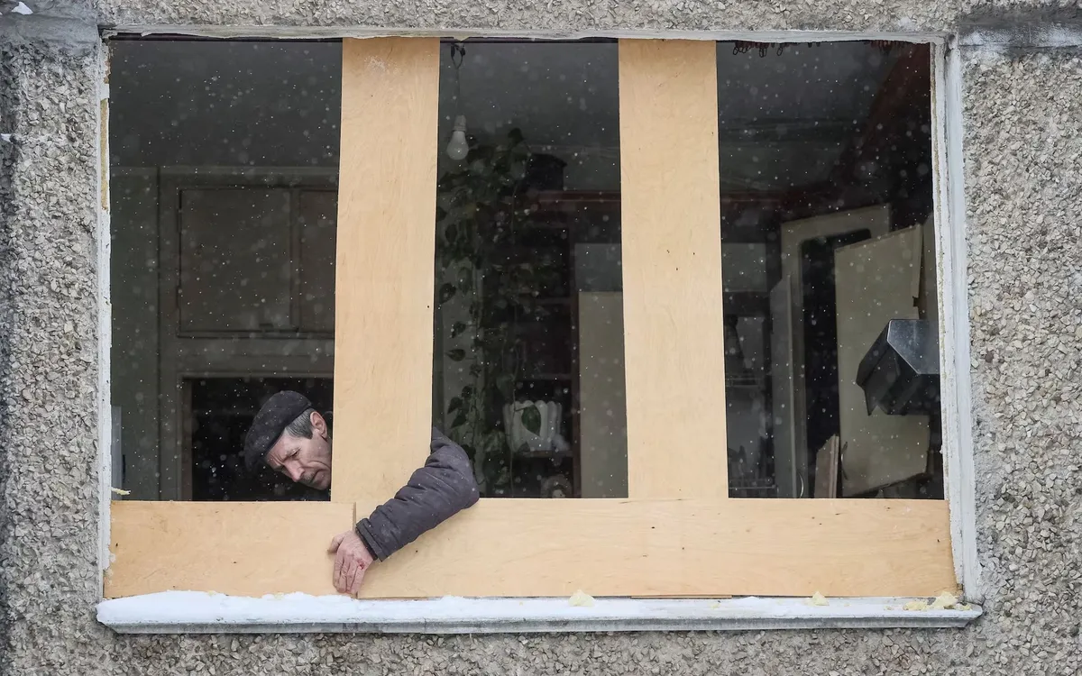 Người đàn ông lắp ván OSB thay cửa sổ bị vỡ sau cuộc tấn công bằng thiết bị bay không người lái của Nga tại Kiev, Ukraine, ngày 5/2/2026 (Ảnh: Reuters)