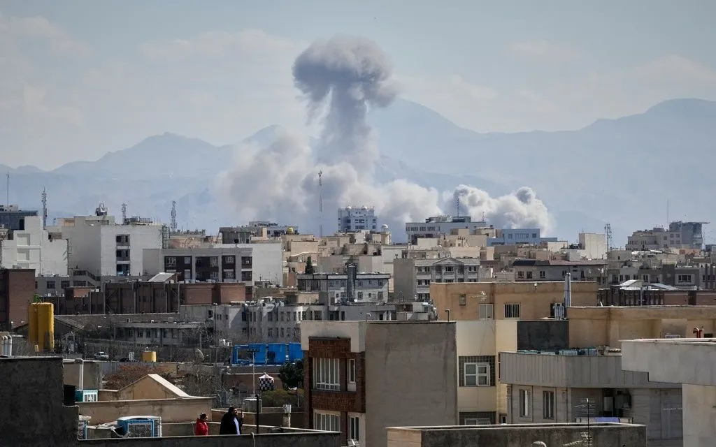 Người dân đứng trên mái nhà quan sát cột khói bốc lên sau một vụ không kích tại Tehran, Iran, ngày 1/3/2026. (Ảnh: AP/Vahid Salemi)