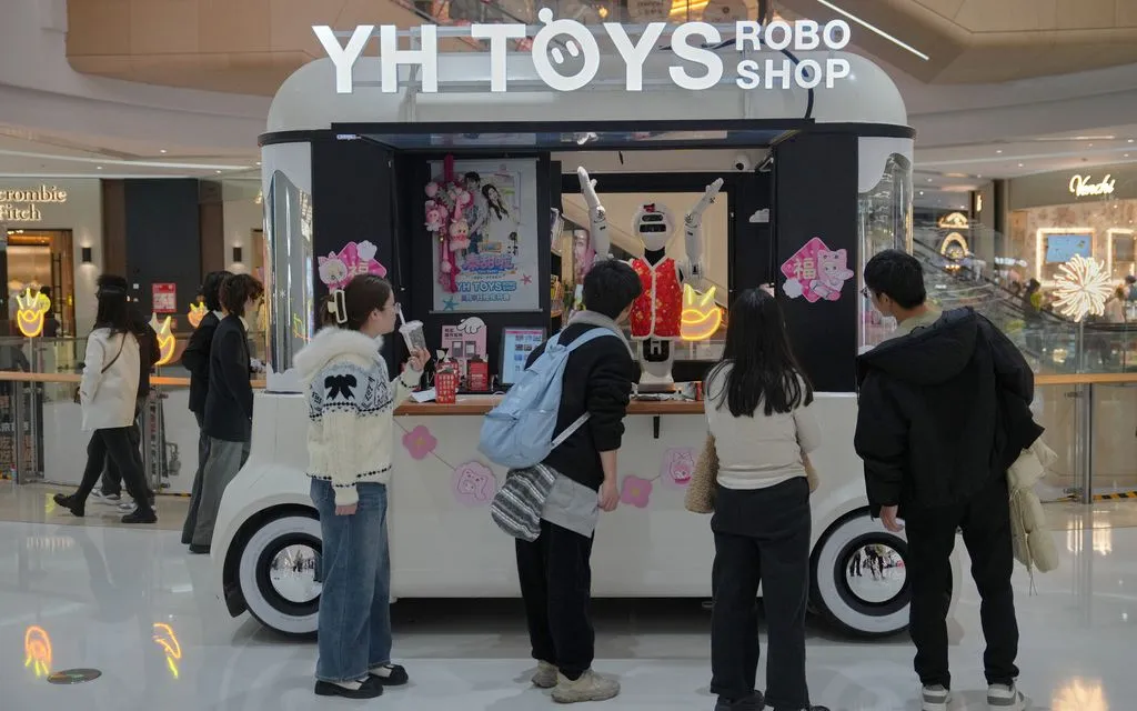 Người mua sắm xem robot hình người mặc váy đỏ bán đồ chơi tại một trung tâm thương mại ở Bắc Kinh, Trung Quốc, ngày 28/2/2026. (Ảnh: AP)