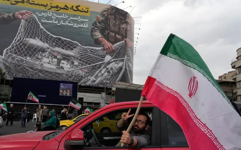 Người đàn ông giương cờ Iran trước tấm áp phích chống Mỹ tại trung tâm Tehran, Iran. (Ảnh: AP)