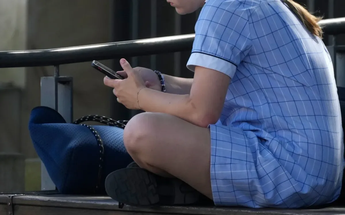 Một thiếu nữ sử dụng điện thoại khi ngồi trên ghế tại Sydney ngày 8/11/2024. (Ảnh: AP)