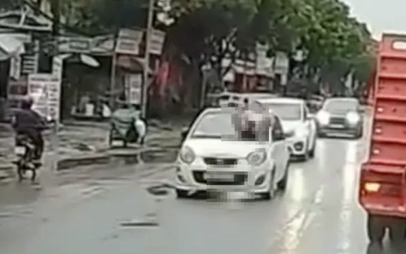 Hình ảnh người đàn ông nằm trên nắp capo ô tô chạy trên đường. (ảnh: Cắt từ Clip)