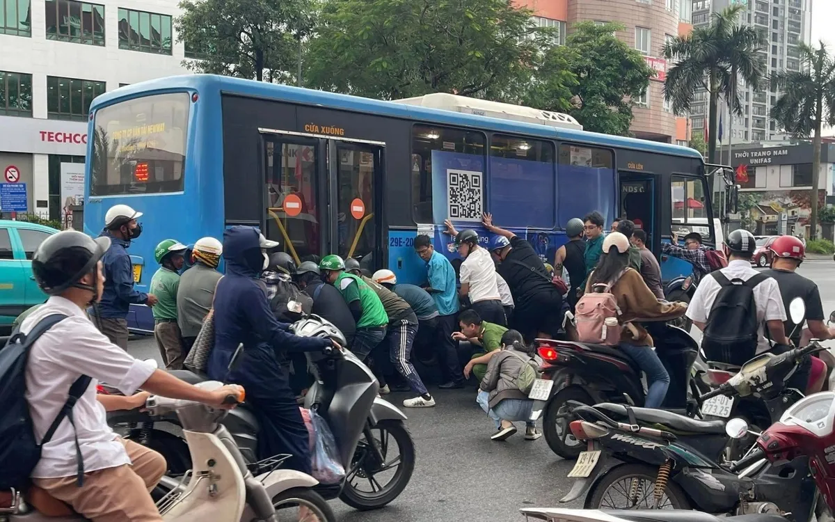 Người dân cùng lực lượng chức năng nâng xe buýt cứu  nữ tài xế mắc kẹt dưới gầm. (ảnh: Viết Tường)