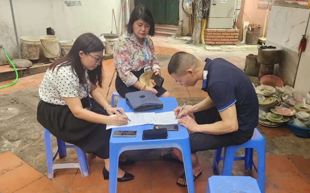 Lực lượng chức năng lập biên bản xử phạt quán cơm vi phạm an toàn thực phẩm và lấn chiếm ngõ đi. Ảnh: Phường Cầu Giấy