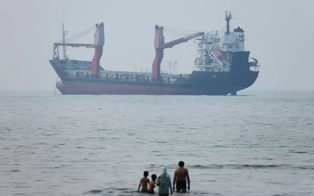 Người dân đứng dưới vùng nước nông gần một tàu hàng neo đậu ở eo biển Hormuz, ngoài khơi Bandar Abbas, Iran, ngày 30/6/2026 (Ảnh: ISNA/AP)