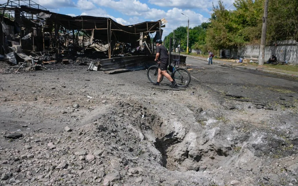 Một người đàn ông đi qua hố tên lửa tại khu chợ bị phá hủy ở Kiev, Ukraine, ngày 30/7/2026 (Ảnh: AP)