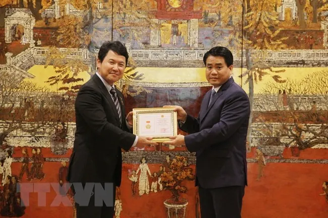Chairman of the municipal People’s Committee Nguyen Duc Chung (R) presents “for the cause of capital city construction” insignia to Katsuro Nagai, Japanese Deputy Ambassador in Vietnam (Photo: VNA)