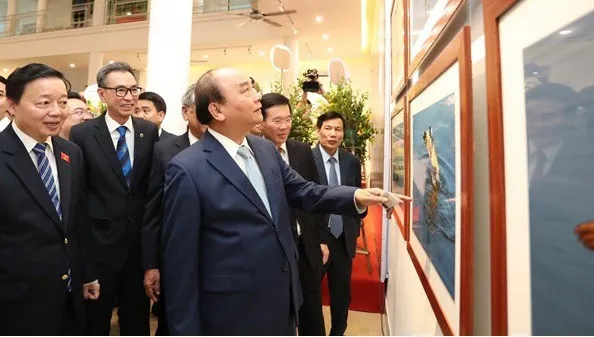 Prime Minister PM Nguyen Xuan Phuc joins other delegates to admire photos on display at the exhibition (Photo: hanoimoi.com.vn)