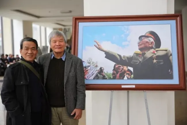 Journalists Nguyen Dinh Toan (right) and Tran Dinh beside the photo titled 'General Vo Nguyen Giap waving to Dien Bien for the last time'. (Photo: thethaovanhoa.vn)