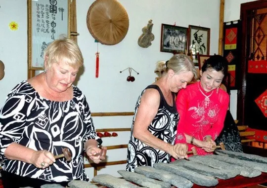 Meritorious Artist Tuyet Mai shows international tourists how to play a traditional Vietnamese musical instrument at Truc Mai Home Concert. (Photo courtesy of www.nld.com.vn)