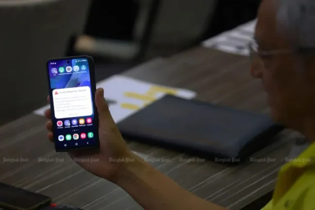A man looks at an alert displayed on a mobile phone. Telecom operators and regulators on Friday jointly tested a virtual cell broadcast entity system for use in emergency situations such as earthquakes. (Photo:Bangkok Post)