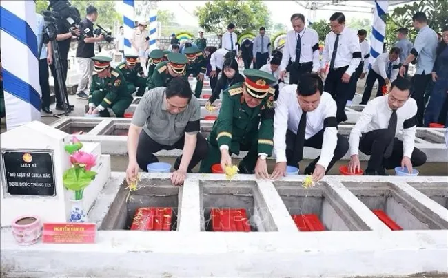 PM Pham Minh Chinh (first, left) and officials scatter flowers and earth to rebury martyrs' remains at the ceremony at the Doc Ba Dac cemetery in Thoi Son ward, An Giang province, on July 21. (Photo: VNA)