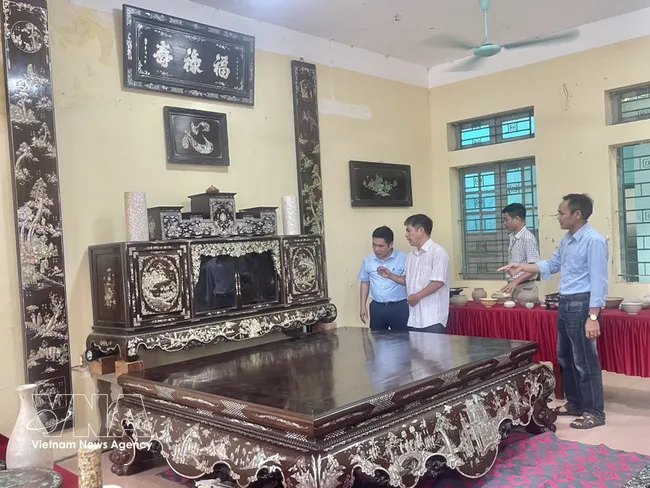 Artisan Vu Van Vinh from Chuyen My commune introduces to visitors a set of mother of pearl inlaid lacquer furniture including a platform bed, tea cabinet, and lacquered horizontal boards and parallel sentences made by his family, worth more than 3 billion VND. (Photo: VNA)